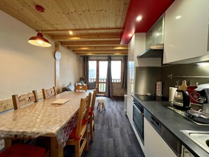 A cozy kitchen with wooden cabinets, a dining table with chairs, and a view to the outside. - Warm and cozy apartment, 250 m from the slopes, fully renovated, sleeps 6 (La Plagne Tarentaise)
