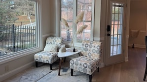 A cozy seating area with two armchairs and a small table, a large window with a view of the outdoors, and a door leading to another room.