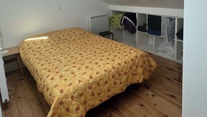 Een slaapkamer met een bed, houten vloer, witte muren, een dakraam en een inbouwkast.