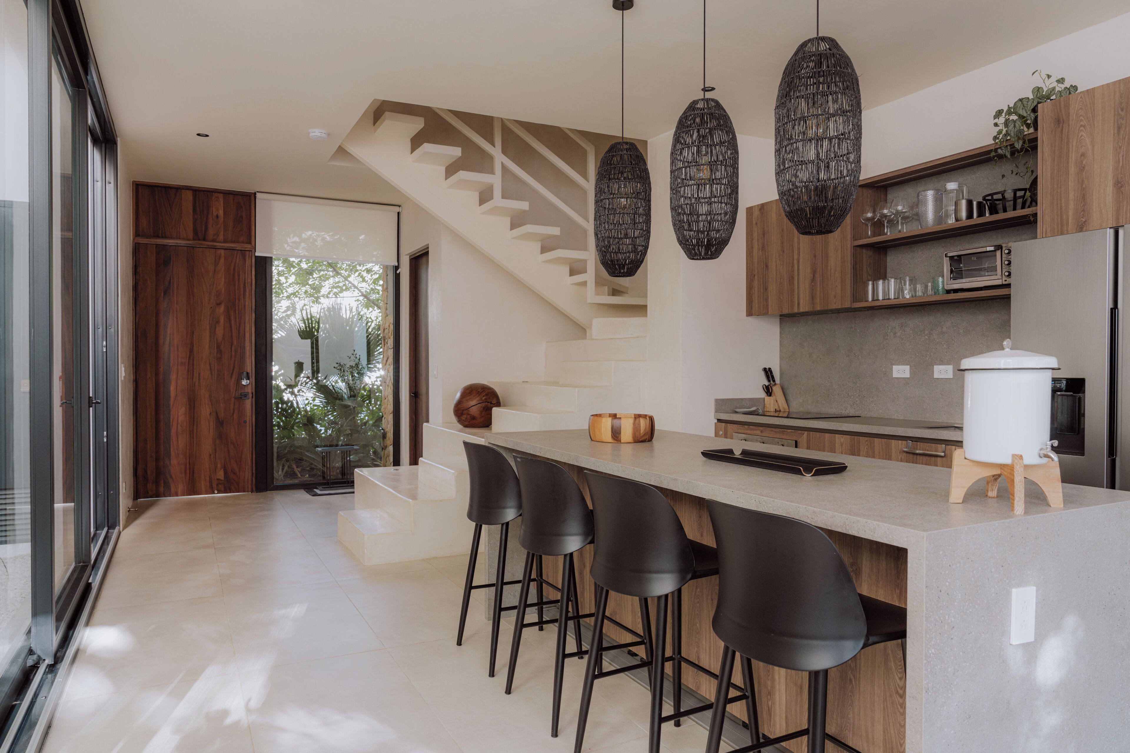 A modern kitchen with a central island, bar stools, a built-in oven, and a staircase leading to an upper level.