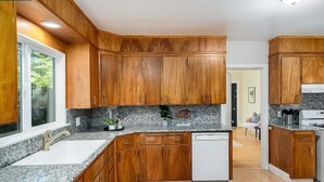 Cocina con armarios de madera, encimeras de granito, lavavajillas y una ventana.