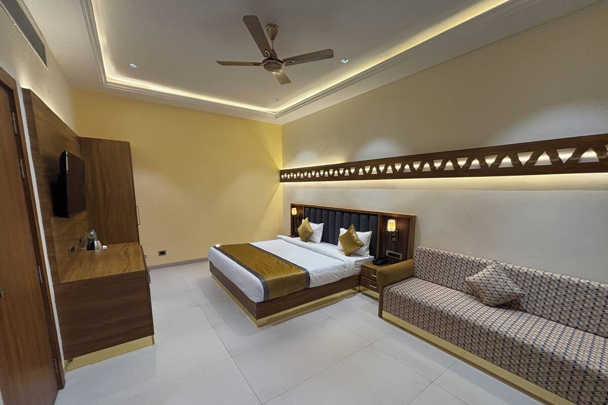 A bedroom with a bed, a sofa, a ceiling fan, and a TV.