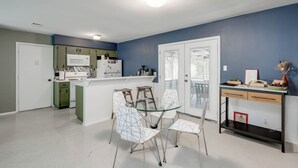 Una cocina moderna con armarios blancos, una mesa de comedor de vidrio y sillas. Hay un refrigerador blanco, un microondas y una cafetera.