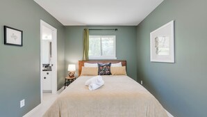 Un dormitorio con cama, una mesita de noche, una ventana con cortinas e imágenes enmarcadas en las paredes.