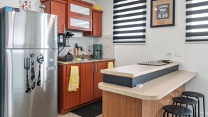 Una cucina compatta con frigorifero in acciaio inox, mobili in legno, una macchina da caffè e un piccolo angolo bar con sgabelli.