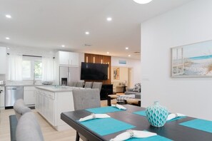 A modern kitchen with white cabinets, a dining area with a table set for two, and a living area with a sofa and a flat-screen TV. - Large tropical group retreat | Beach just steps away | Spacious modern home (Nassau)