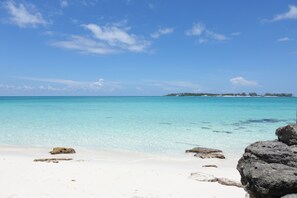 Uma praia com águas turquesa cristalinas, areia branca e algumas rochas espalhadas.