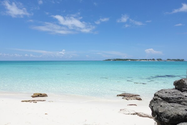 A beach with clear turquoise water, white sand, and scattered rocks. - Large tropical group retreat | Beach just steps away | Spacious modern home (Nassau)