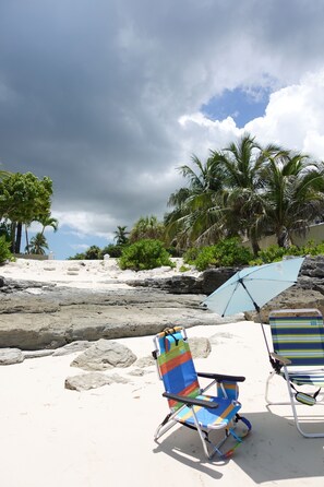 A beach with two striped beach chairs and a blue umbrella. - Large tropical group retreat | Beach just steps away | Spacious modern home (Nassau)