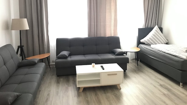 Ein modernes Wohnzimmer mit einem grauen Sofa, einem weißen Couchtisch und einem Bett mit einem gestreiften Kissen.
