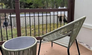 A wicker chair and table on a wooden deck with a railing and stone wall in the background. - Heated Pool, Fire Pit & Forest Views  Poconos (Palmyra Township)