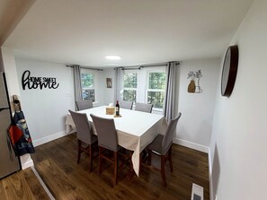 A dining area with a table set for four, wooden flooring, and a view through the windows. - Heated Pool, Fire Pit & Forest Views  Poconos (Palmyra Township)