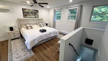 Een slaapkamer met een bed, nachtkastjes, een plafondventilator, een open haard en uitzicht op groen.