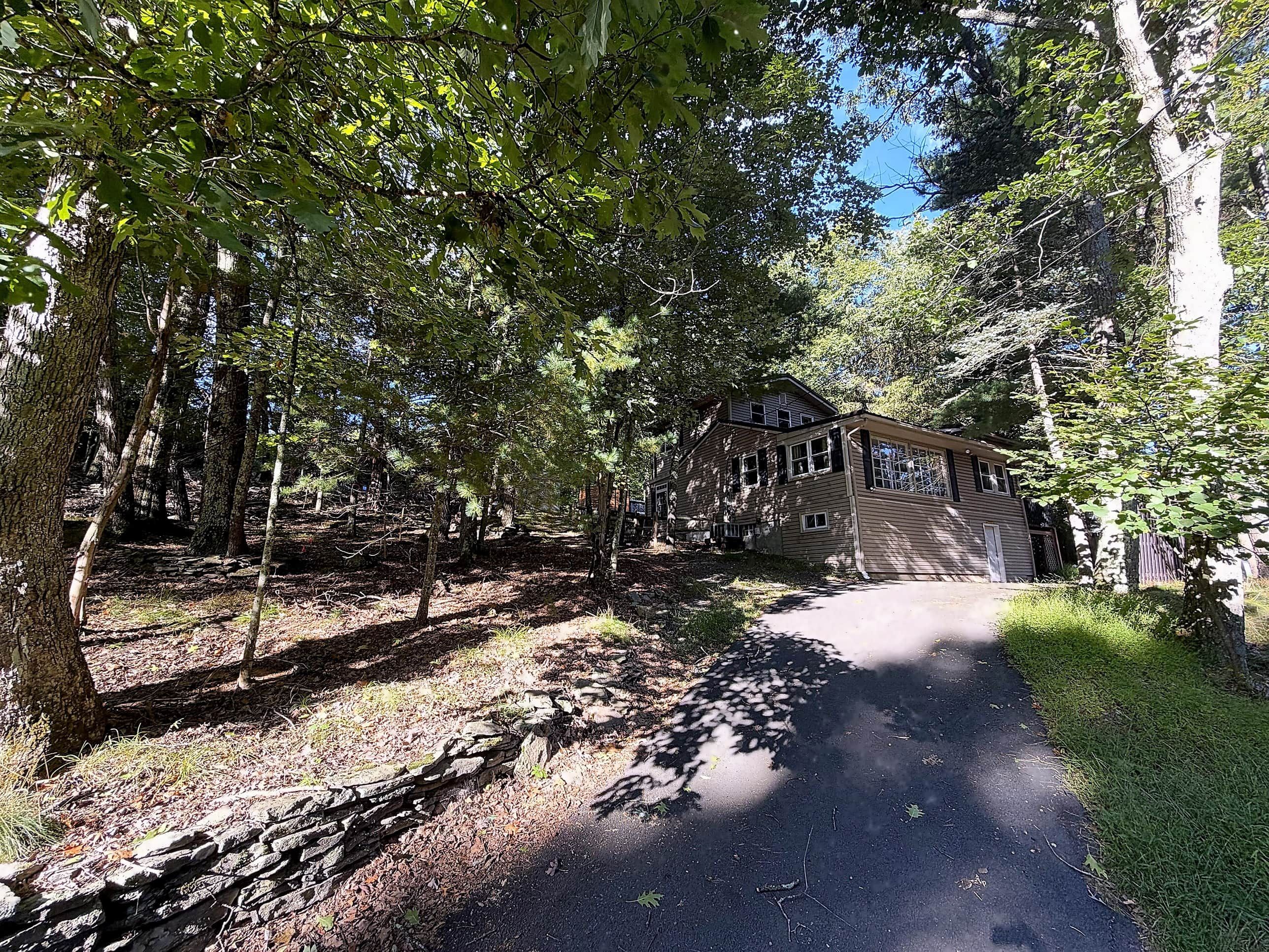 A two-story house surrounded by trees with a paved driveway leading to the entrance.