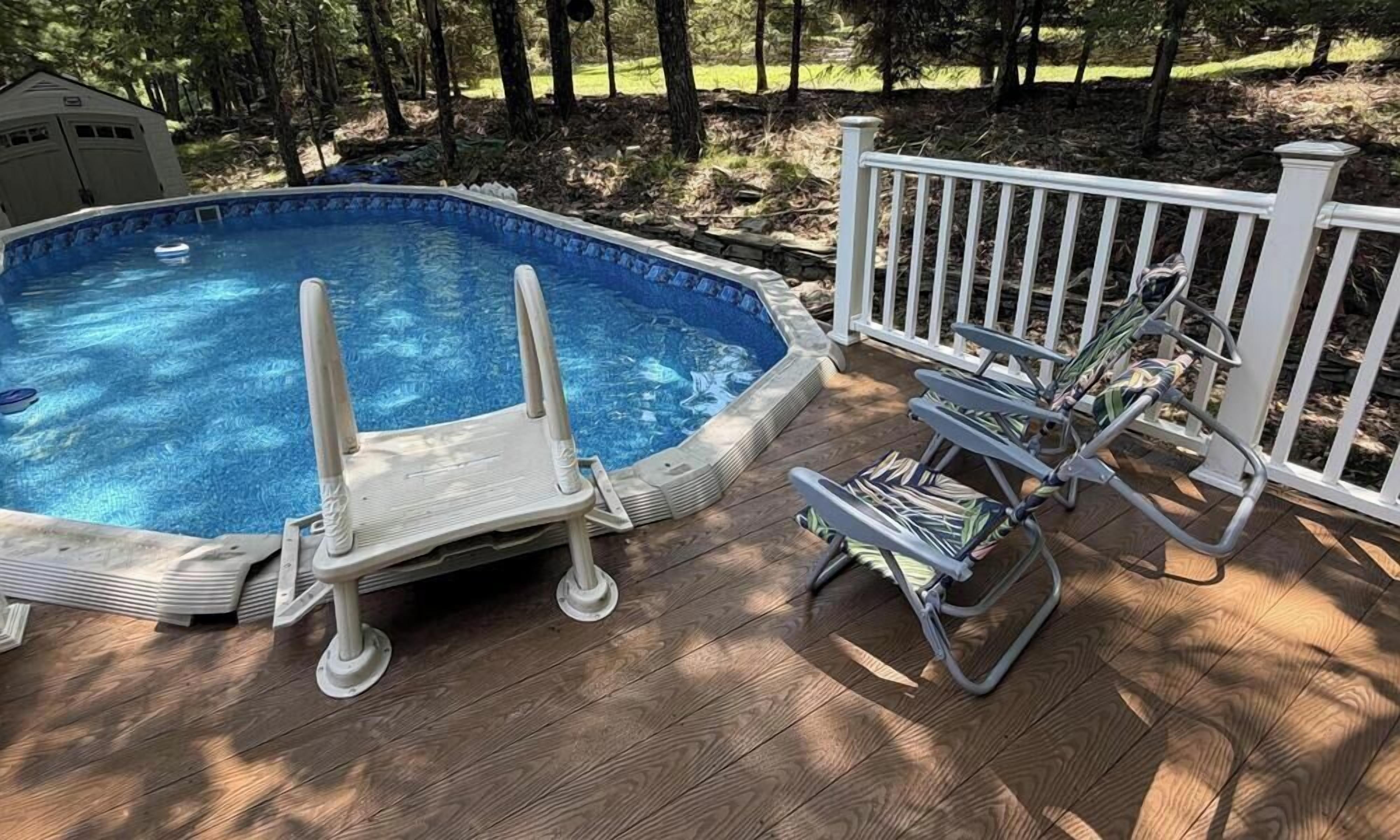 Piscina externa com deck de madeira, cerca branca e uma espreguiçadeira.