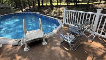 Piscina externa com deck de madeira, cerca branca e uma espreguiçadeira.