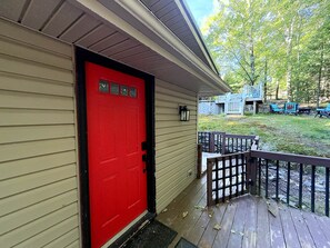 Une porte rouge, une terrasse en bois et un mur de pierre en arrière-plan.