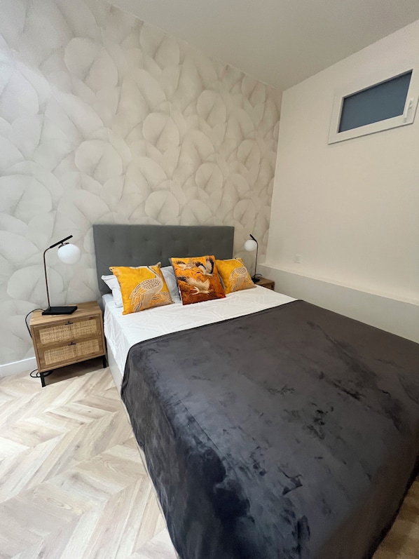 A bedroom with a bed, a nightstand, a wall-mounted shelf, and a small window.