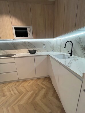 A modern kitchen with a microwave, two sinks, and a herringbone wood floor.