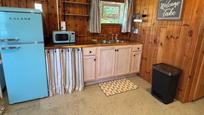 Eine kleine Küche mit Holzwänden, einem blauen Kühlschrank, einer Mikrowelle, einem Spülbecken und einem Mülleimer.