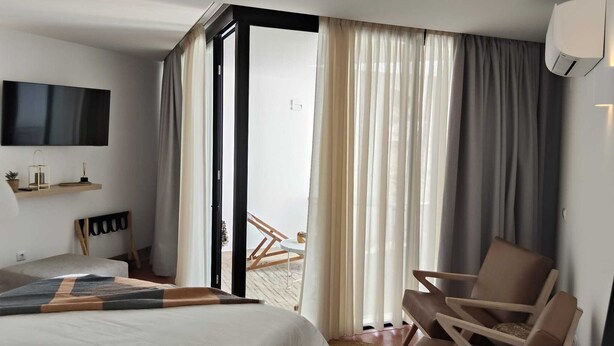 Une chambre d’hôtel avec un lit, une chaise, une télévision et une vue sur l’extérieur, visible à travers une porte vitrée.