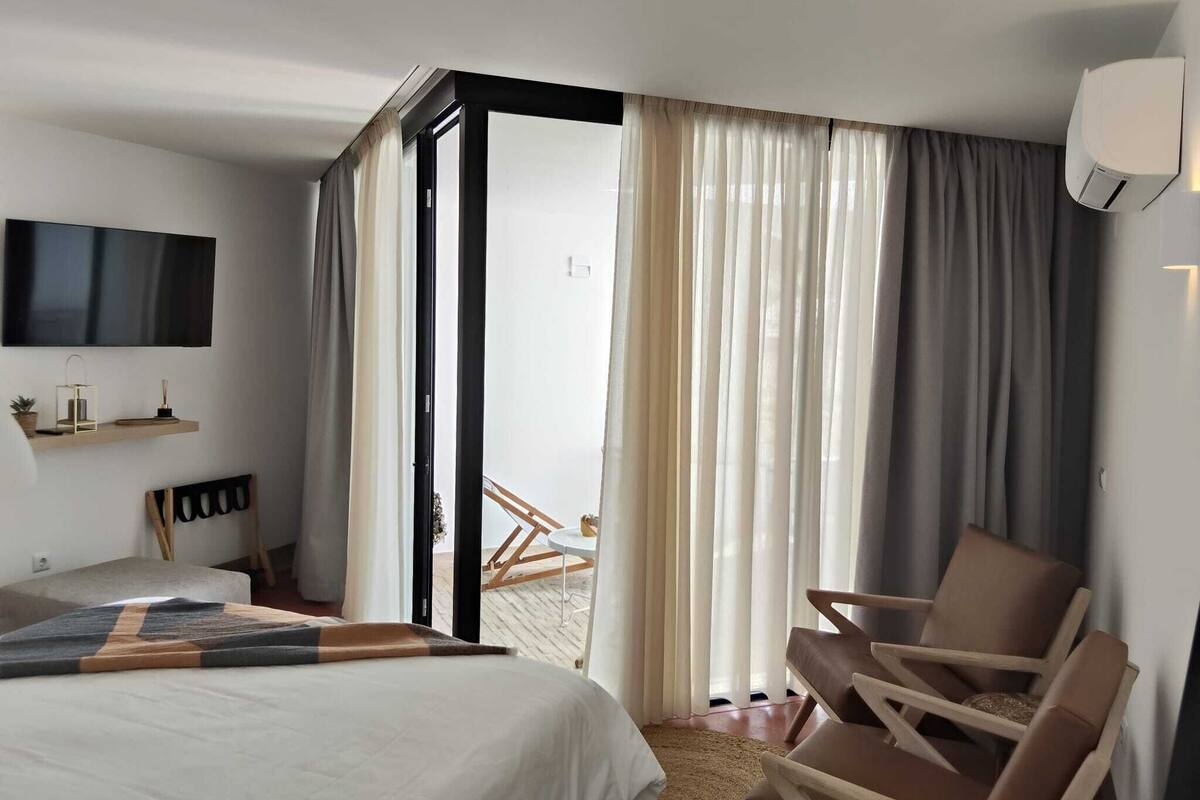 Een hotelkamer met een bed, een stoel, een televisie en uitzicht door een glazen deur.