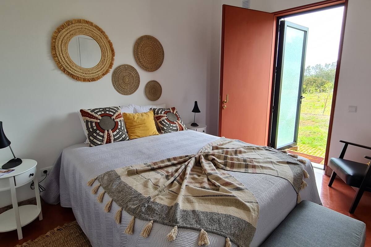 Een slaapkamer met een bed, nachtkastje, lamp, raam en een deur naar buiten.