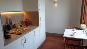 Une cuisine moderne avec des meubles blancs, un plan de travail en bois, une bouilloire rouge et un coin repas comprenant une table blanche et des chaises rouges.