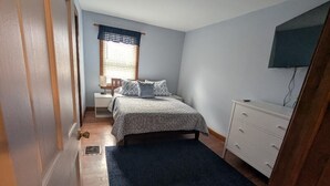A bedroom with a bed, bedside table, dresser, and a window with blinds.