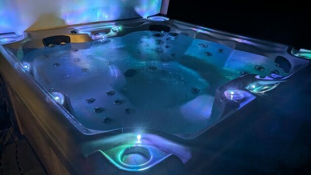 A hot tub with built-in lighting and a wooden bench.