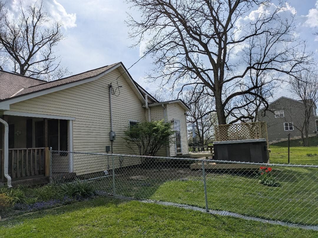 A residential house with a fenced yard, a garage, and a tree in the background.