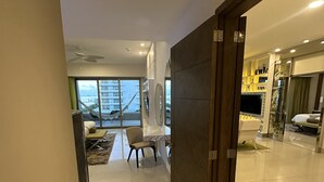 Quarto de hotel moderno com uma janela grande, televisão de tela plana e área de estar com uma cadeira e uma mesa pequena.