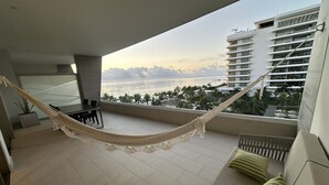 Uma varanda com rede, sofá e vista para o mar e palmeiras.