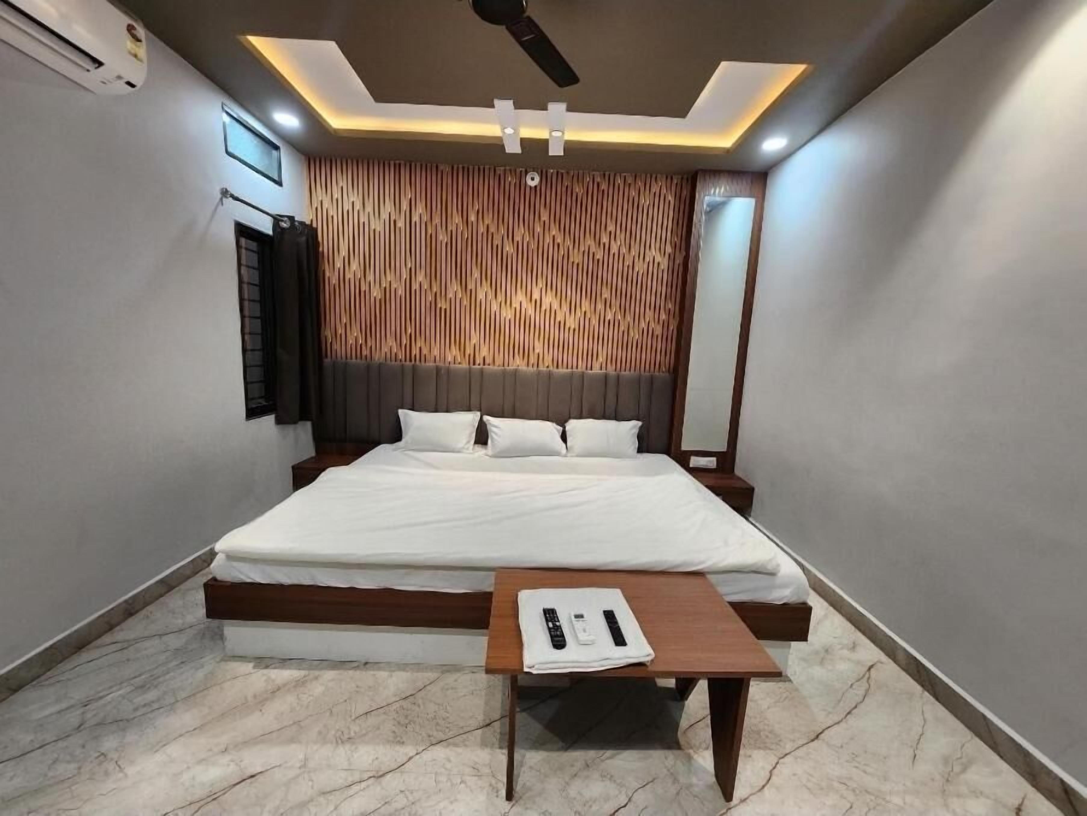 A modern bedroom with a large bed, a bedside table with a remote control, and a ceiling fan.