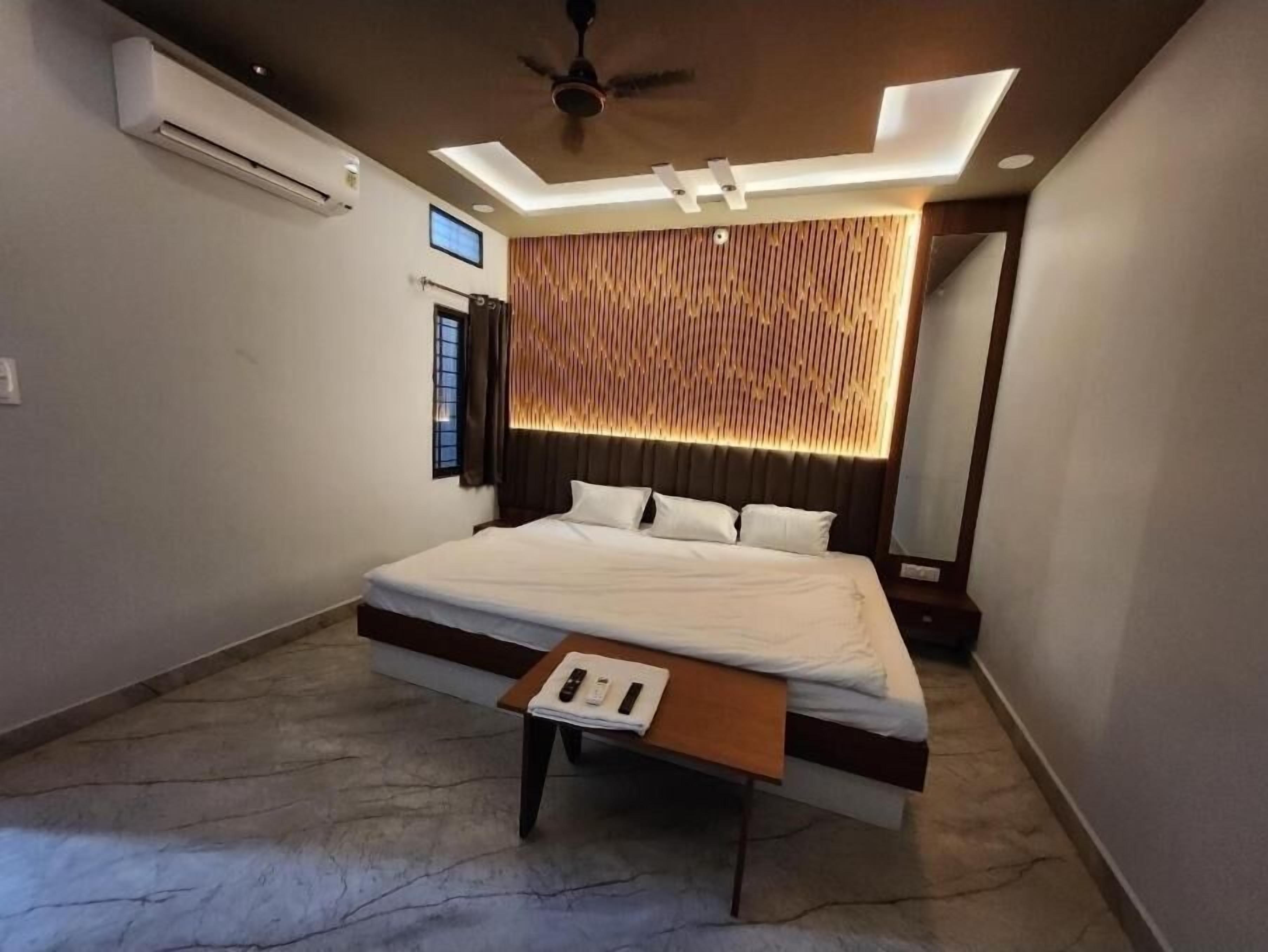Quarto moderno com uma cama grande, ventoinha no teto, iluminação embutida, parede de destaque em madeira e uma pequena mesa de cabeceira.