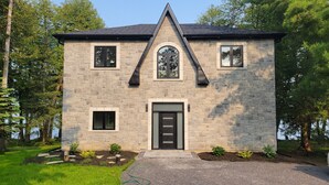 A stone house with a black roof, a central arched window, and a black front door.