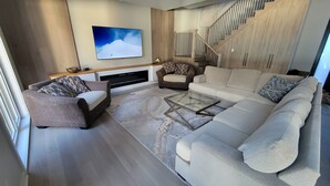 A modern living room with a sectional sofa, a glass coffee table, and a flat-screen TV mounted on the wall.