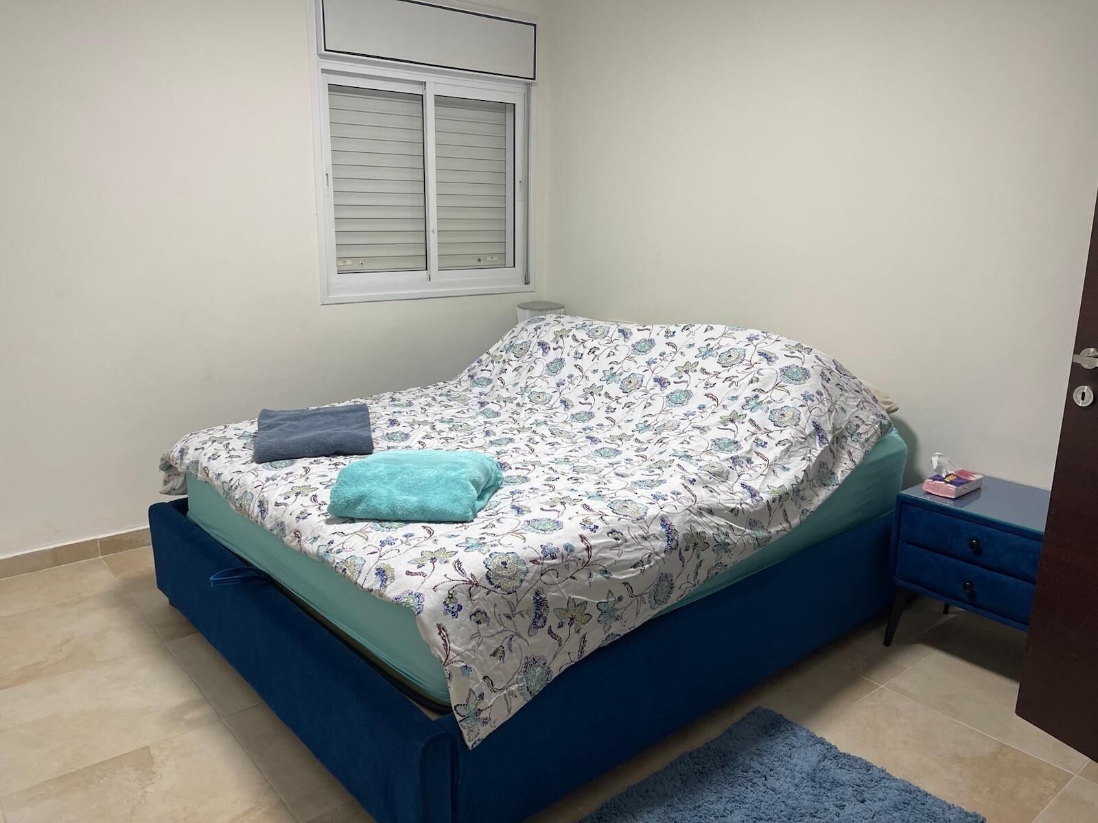 A bedroom with a bed, a window, a nightstand, and a door.
