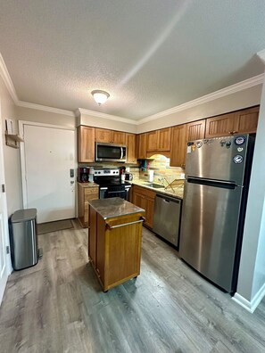 A compact kitchen with wooden cabinets, a stainless steel refrigerator, a microwave, and a stove. - HHI Beach Retreat - Renovated & Ready to Relax (Hilton Head Island)