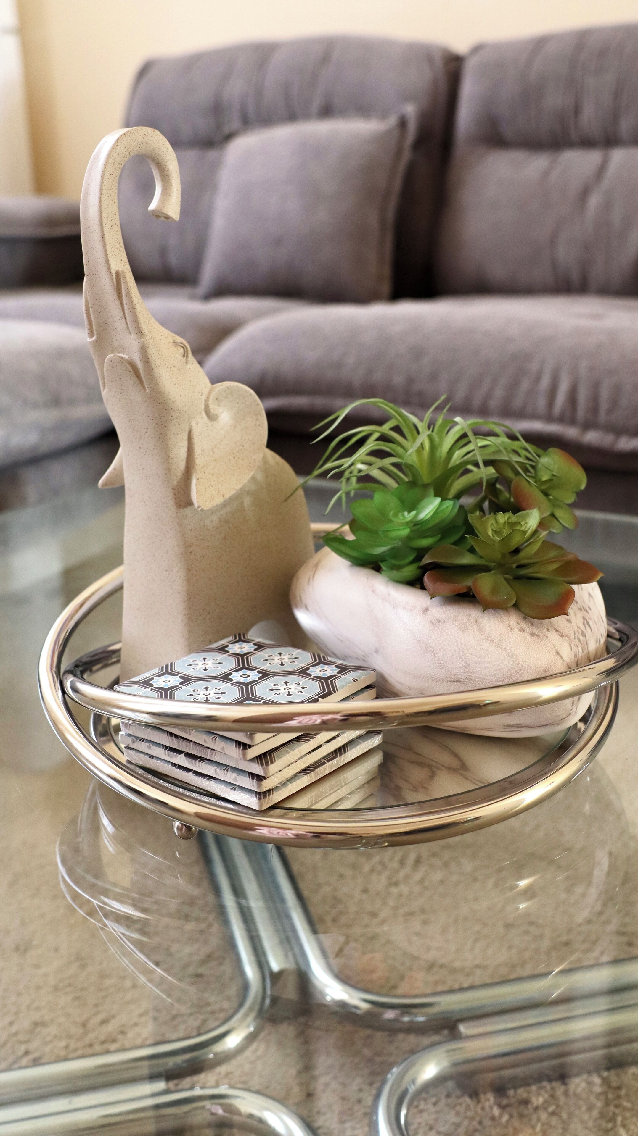 A glass table with a decorative elephant figurine, a succulent plant, and a stack of books.