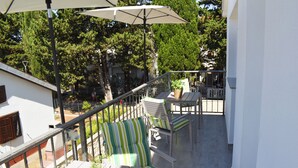 Un balcon agrémenté de meubles d’extérieur, d’une plante en pot et d’un parasol blanc.