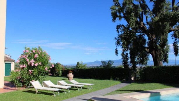 Zona de piscina con sillones de descanso, un árbol grande y vistas a la montaña.
