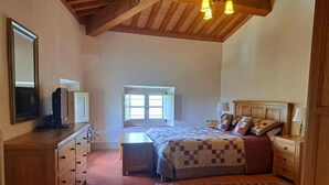 Un dormitorio con una cama, mesitas de noche, cómoda, ventana y techo con vigas de madera.