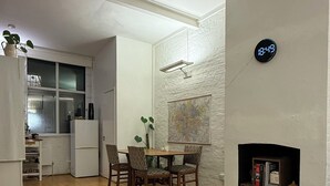 Un salón moderno con comedor, suelo de madera, chimenea y un reloj marcando las 18:49.