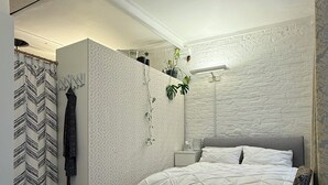 Un dormitorio moderno con cama, una silla, una mesita de noche y una planta colgada en la pared.