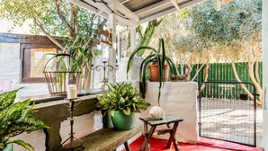 Ein überdachter Patio-Bereich mit Topfpflanzen, einer Bank und einem Tor.