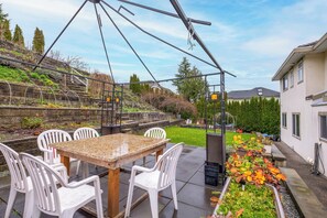 A patio with a table and chairs, a garden with plants, and a house in the background.
