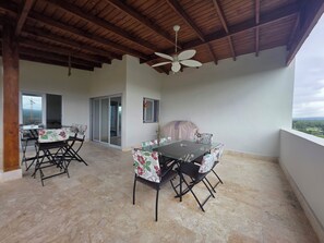 Un patio cubierto con mesa y sillas, ventilador de techo y vistas al paisaje.