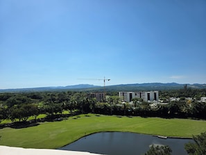 Un campo de golf con un estanque, edificios y montañas al fondo.