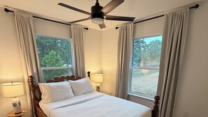 A bedroom with a wooden bed, a ceiling fan, two bedside lamps, and a view of trees through large windows. - Cimarron House in Holly Lake Ranch (Holly Lake Ranch)